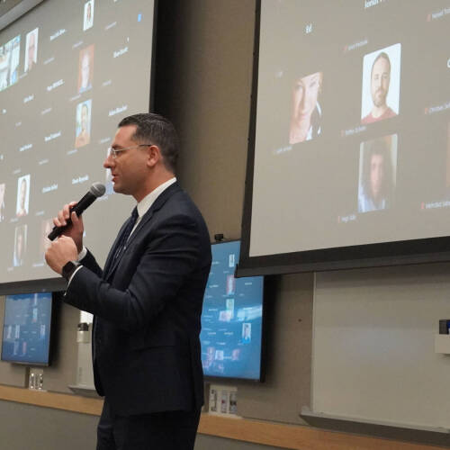 Dean Marouane Kessentini holding a microphone stands against a large digital display featuring a human profile with technology.